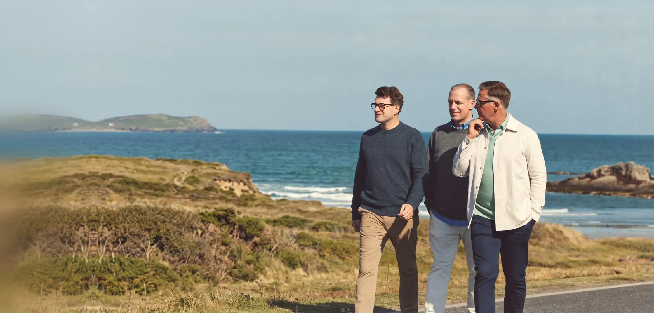 Three men walk a coastal path by the sea