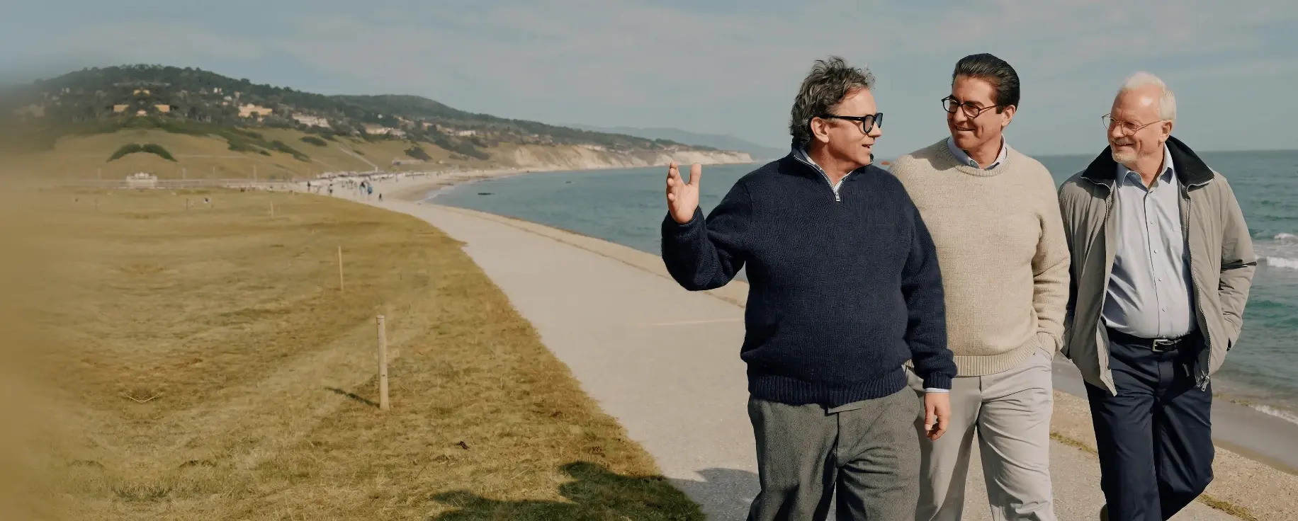 Three men talk as they walk a seafront path