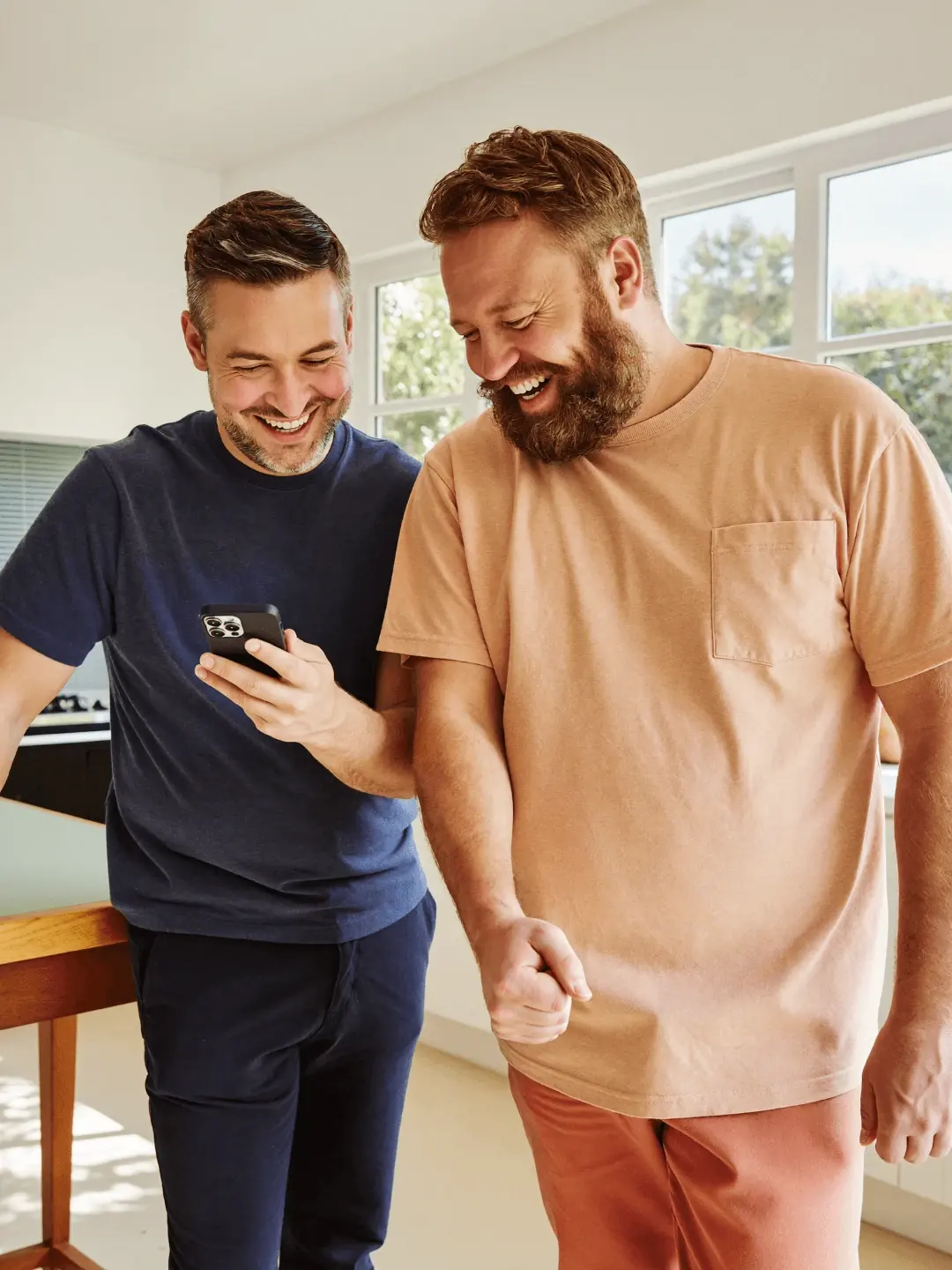 Two men laugh together over a phone at home