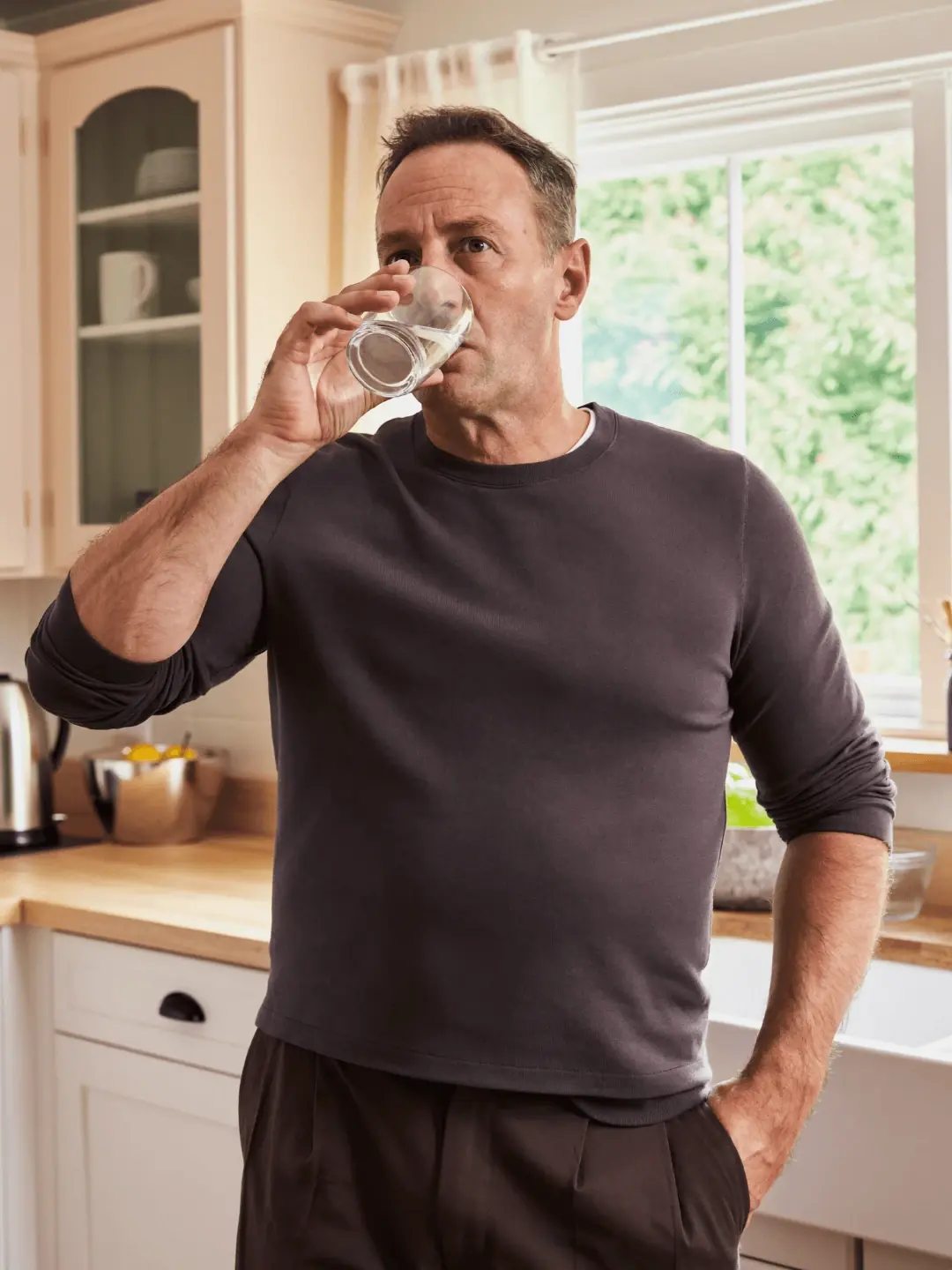 A man drinks a glass of water in his kitchen