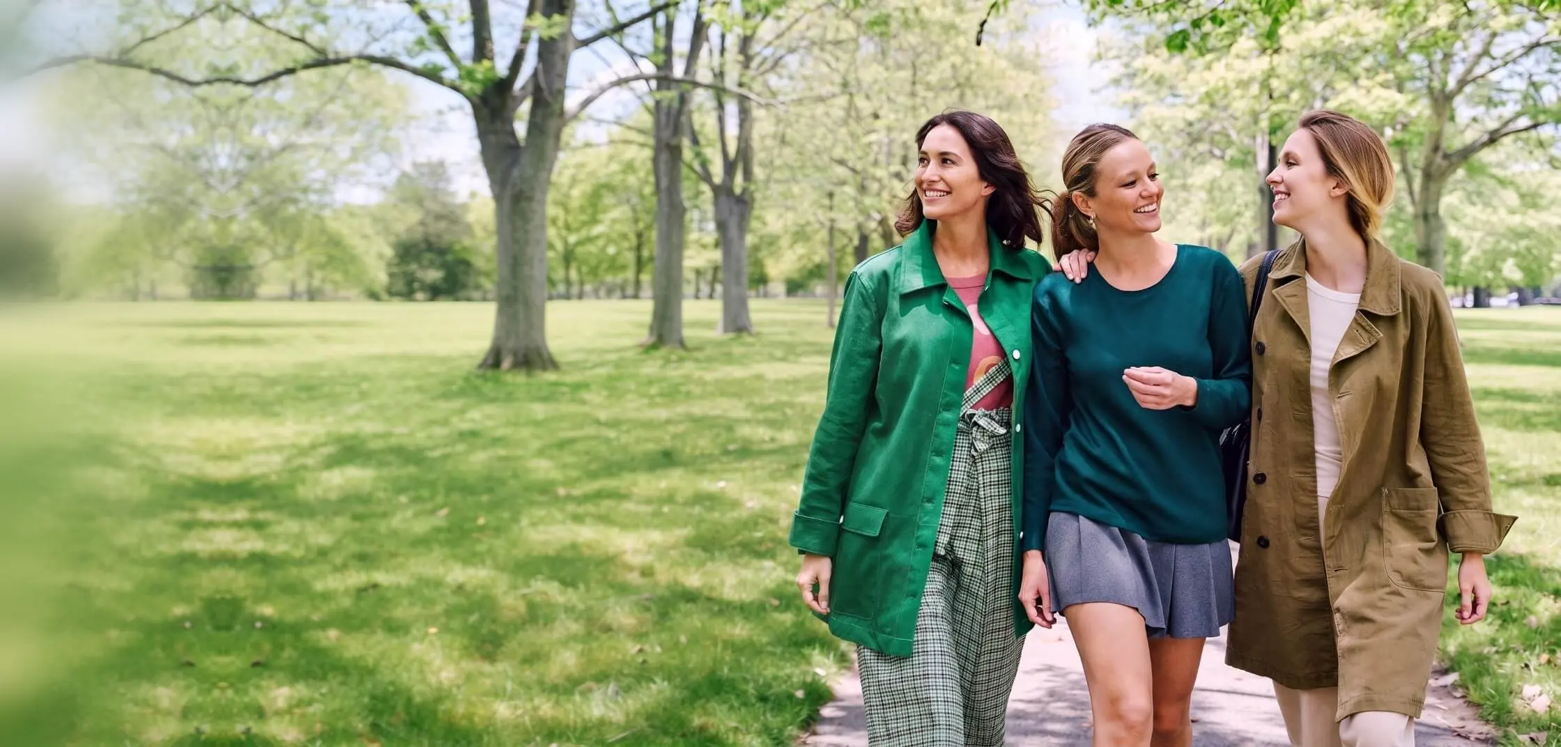 Three women walk arm in arm through a park on a spring day