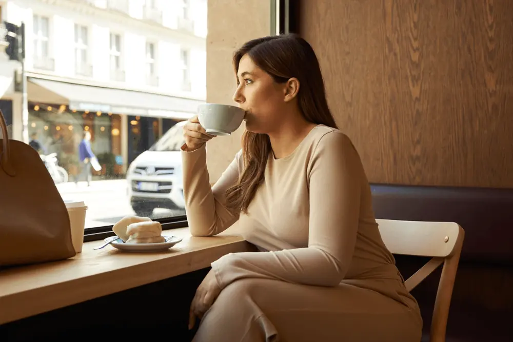 A woman sips a coffee at a café window
