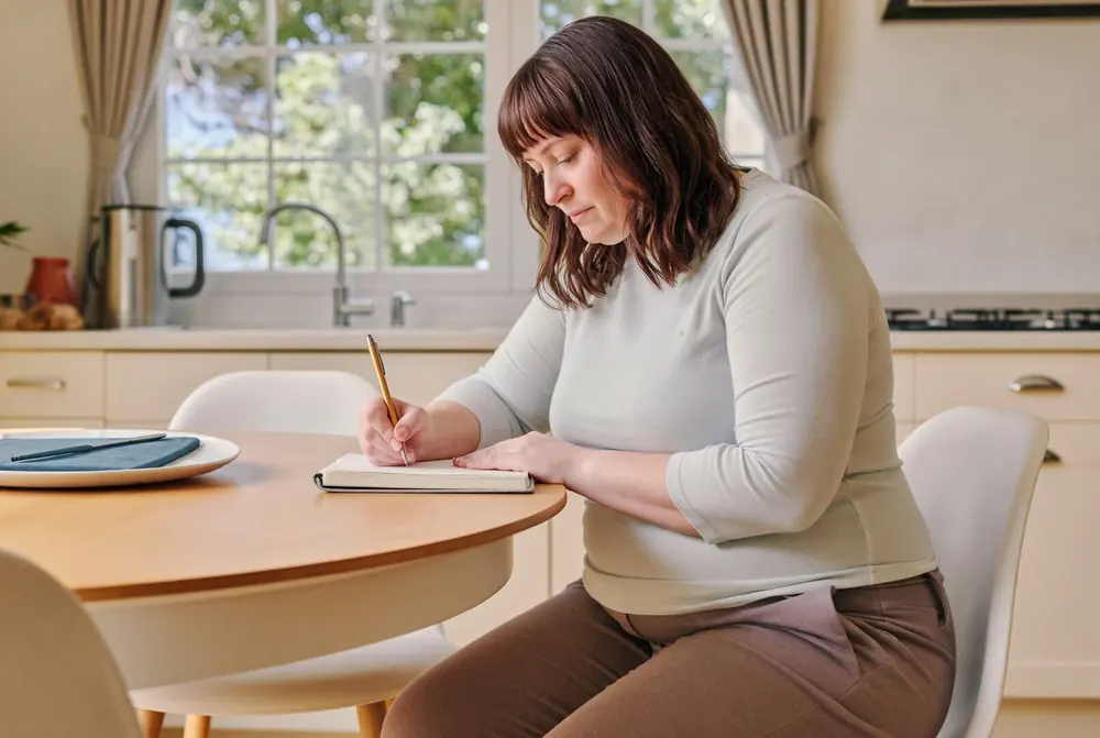 A woman writes in a notebook at her kitchen table
